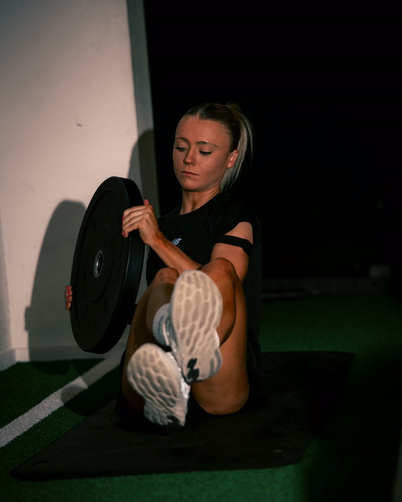 Atlete zit op de mat met een halterschijf in de handen.